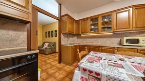 A compact kitchen with wooden cabinets, a microwave, and a dining area with a table covered in a patterned tablecloth.