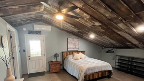 Ein Schlafzimmer mit schrägverdeckter Decke, einem Bett, einem Nachttisch, einer Kommode und einer Tür.