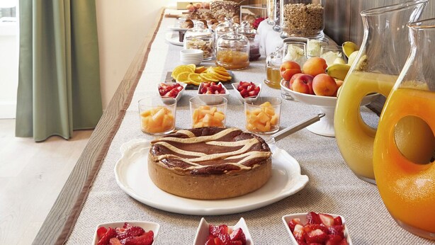 Un bufé de desayuno con diversas frutas, pasteles y una jarra de jugo de naranja.