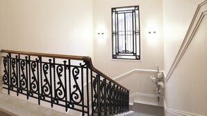 Una imponente escalera con barandales negros decorados, tragaluces y un ventanal con celosía de metal.