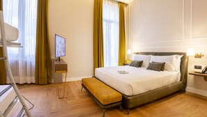 Habitación de hotel ordenada con una cama grande, una mesita de noche, un banco y un televisor sobre un soporte.