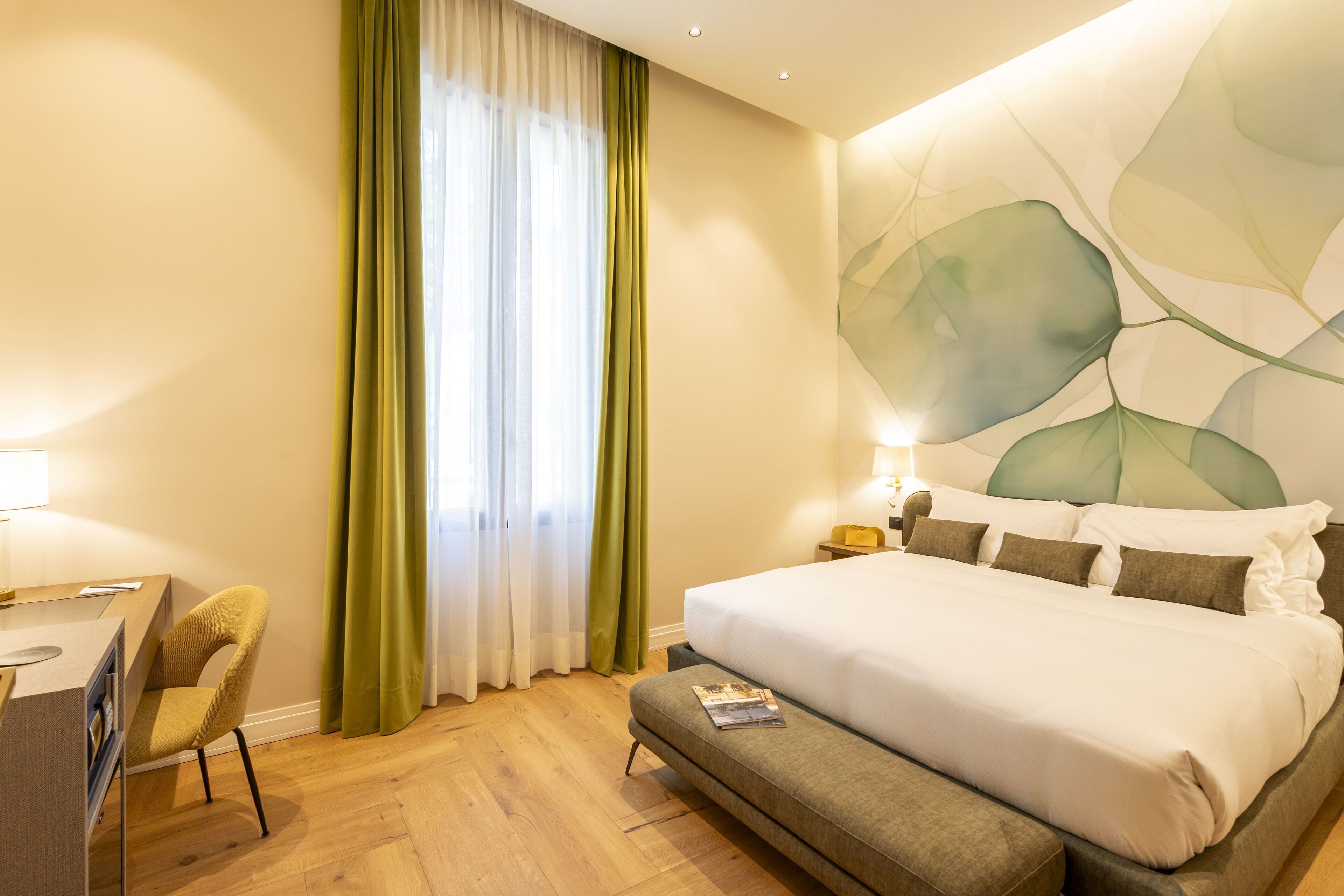 Una habitación de hotel con cama, escritorio, silla y un ventanal con cortinas.