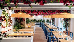 Een restaurant met lange houten tafels en blauwe stoelen, versierd met rode bloemen en groene planten.