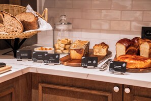 Een bakkerijdisplay met verschillende broden en gebak, waaronder een meergranenbrood en een brioche.