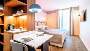 Een hotelkamer met een bed, nachtkastje en een bureau met stoel. Er is een raam met gordijnen, een aan de muur bevestigde televisie en een plafondlamp.