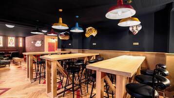 Interior de restaurante com mesas de madeira e banquetas pretas, luminárias pendentes e cabeças de animais decorativas na parede.