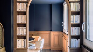 Een gezellig hoekje om te lezen met een houten bankje en boekenplanken vol boeken, een raam voor natuurlijk licht, en een blauw accentmuur.