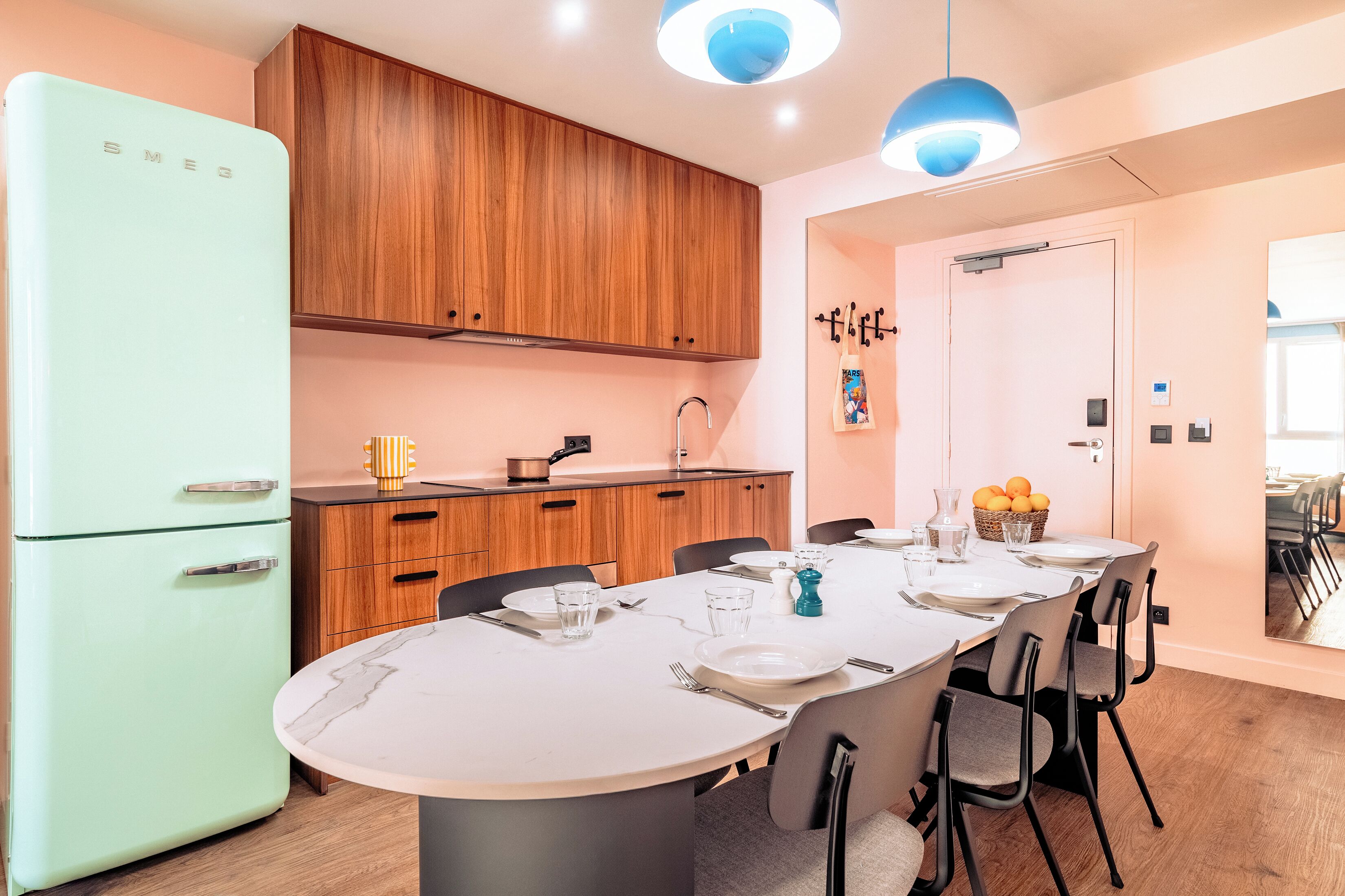 Eine moderne Küche mit einem retro-Kühlschrank, Holzschränken und einem Essbereich mit Marmortisch und Stühlen.