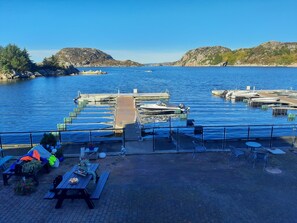 A marina with docked boats, picnic tables, and a clear view of the water and hills in the background. - Fantastic fishing hut with sea view directly on the water (Korshamn)