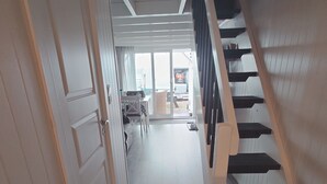 Een gang met een houten trap, een eethoek en uitzicht op buiten.