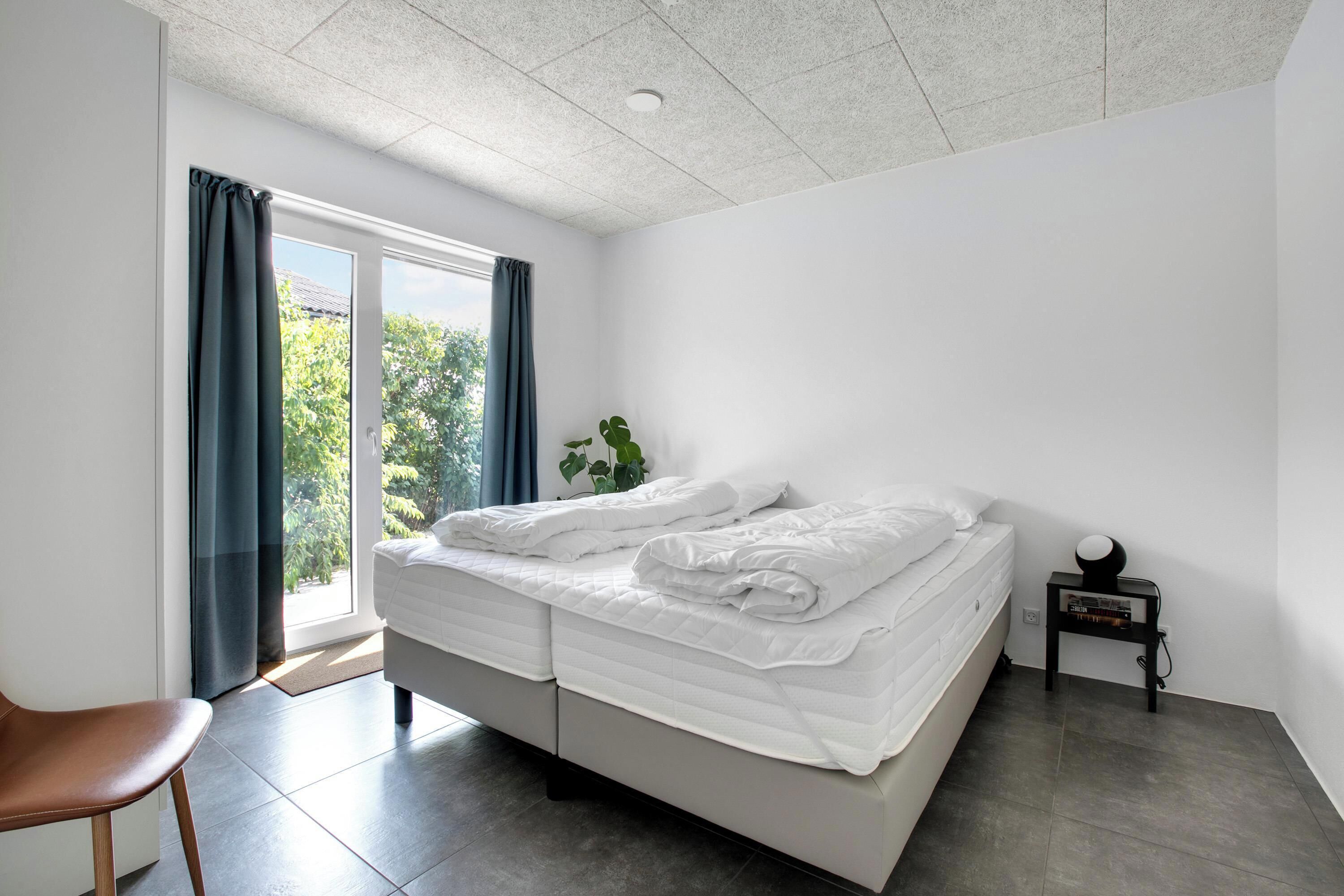 Een moderne slaapkamer met een groot bed, een klein nachtkastje, een stoel en uitzicht op groen.
