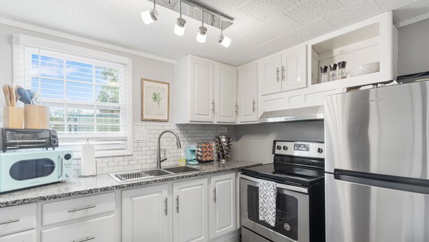 A modern kitchen with white cabinets, stainless steel appliances, a toaster, and a window with blinds.