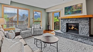 Un salon chaleureux avec une cheminée en pierre, deux fauteuils, un canapé et une table basse.