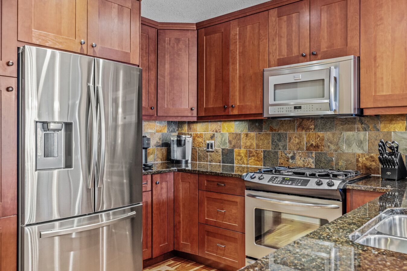 A kitchen with wooden cabinets, a stainless steel refrigerator, a microwave, a stove, and a coffee maker.