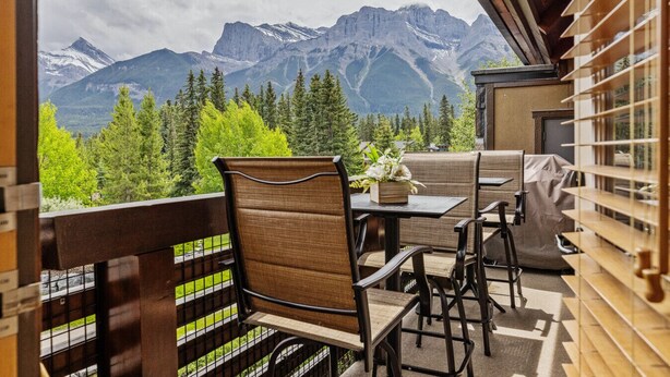 Un balcon avec vue sur les montagnes, une table avec des chaises et une plante en pot.