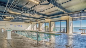 Une piscine intĂ©rieure Ă lâeau claire, dotĂ©e dâun plongeoir et dâun panneau indiquant la prĂ©sence dâun sauveteur.