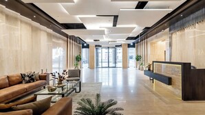 A spacious lobby with a reception desk, leather sofas, and a coffee table. - CaiCai Homes AG Tower Business Bay (Dubai)