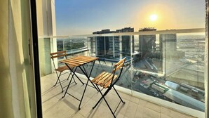 A balcony with two wooden chairs and a table, overlooking a cityscape with buildings and a bridge. - CaiCai Homes AG Tower Business Bay (Dubai)