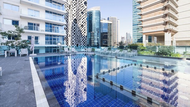 A rooftop swimming pool with a clear view of surrounding modern buildings and a landscaped area with lounge chairs. - CaiCai Homes AG Tower Business Bay (Dubai)