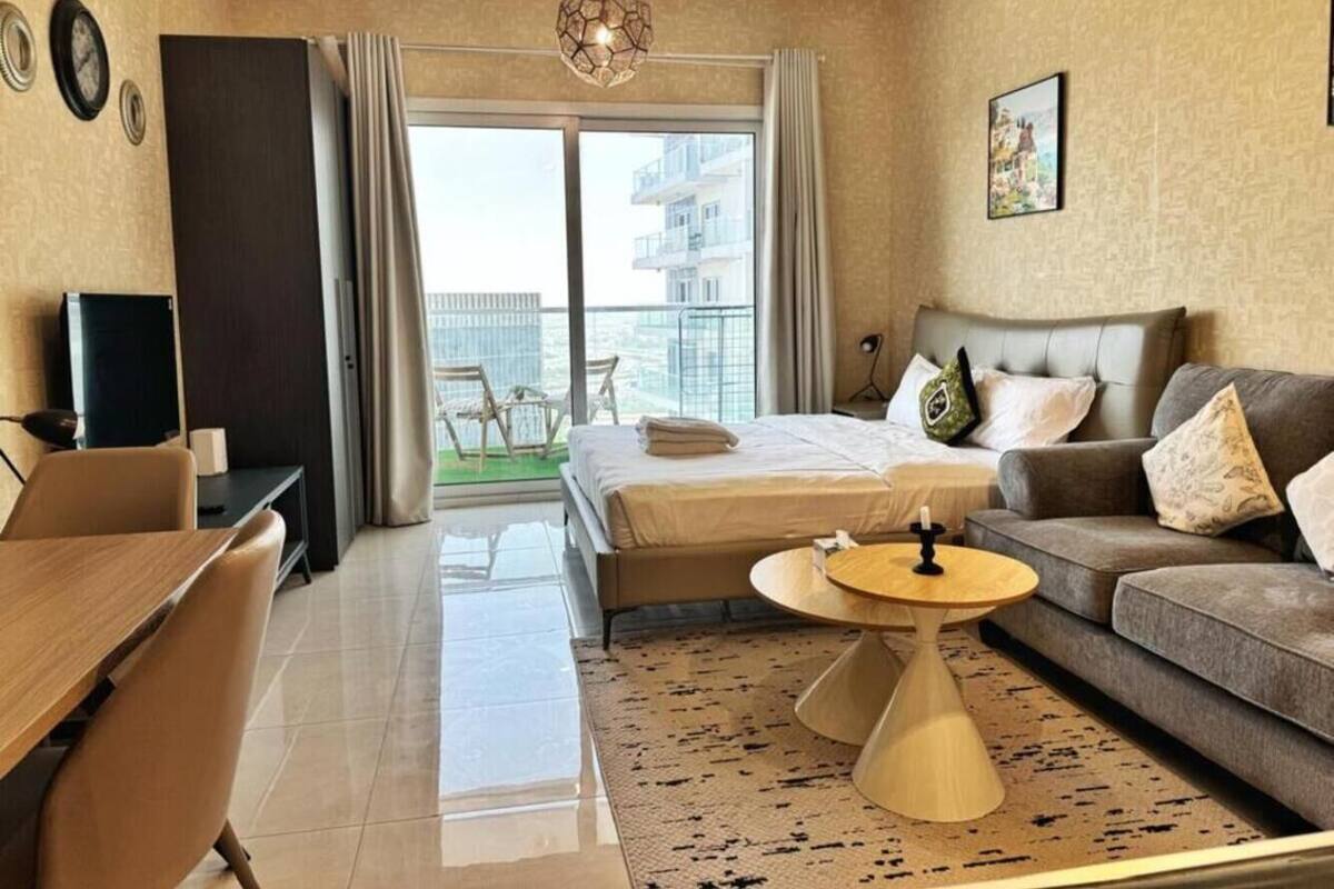 Habitación de hotel moderna con cama, sofá, escritorio y balcón con vistas a edificios.