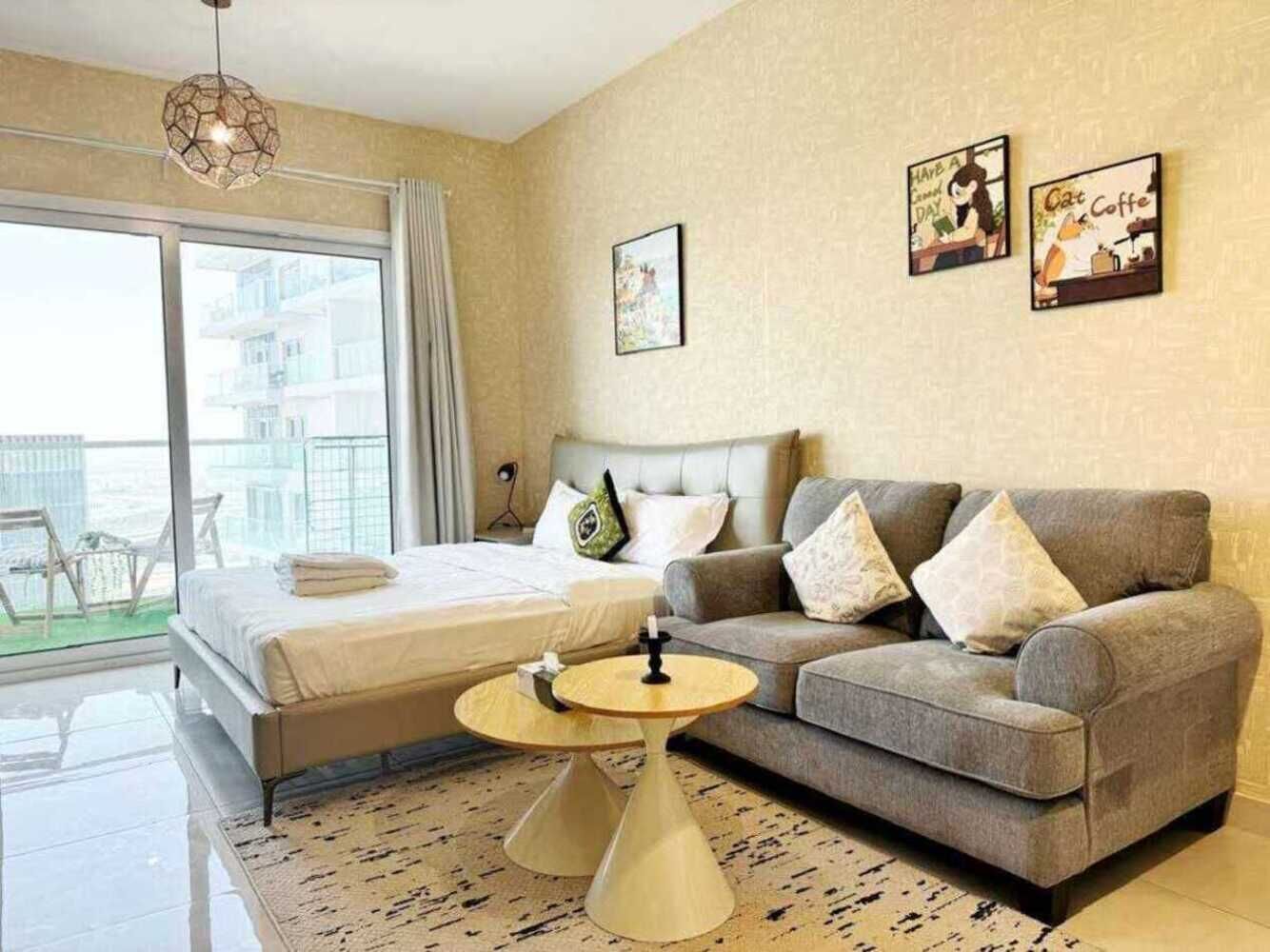 A modern hotel room with a bed, a sofa, a small round table, and a balcony with a view.