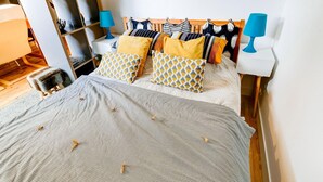 Una cama bien hecha con una colcha estampada, cabecera de madera y varios almohadones de diferentes diseños y colores.