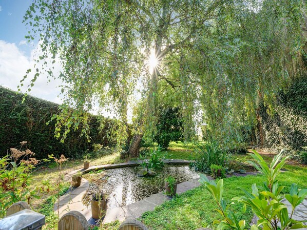 Un jardín con un estanque, rodeado de diversas plantas y una valla de madera.