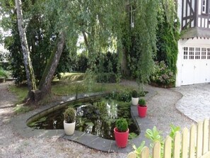 A garden with a pond, potted plants, and a white building with windows. - Romantic Stay, Isigny-sur-Mer (Isigny-sur-Mer)