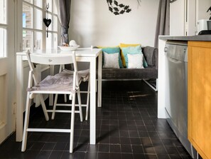 A compact kitchen with a dining area, a sofa with cushions, and a window with curtains. - Romantic Stay, Isigny-sur-Mer (Isigny-sur-Mer)