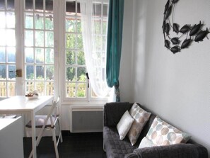 Een kamer met een witte tafel, een donkerbruine bank met gestreepte kussens, een raam met gordijn en een decoratie aan de muur.