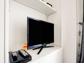 Un televisor sobre un estante blanco, con un control remoto y un reproductor de DVD debajo.