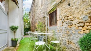 Un patio con un muro de piedra, una mesa y sillas de metal blanco, y un pequeño árbol.