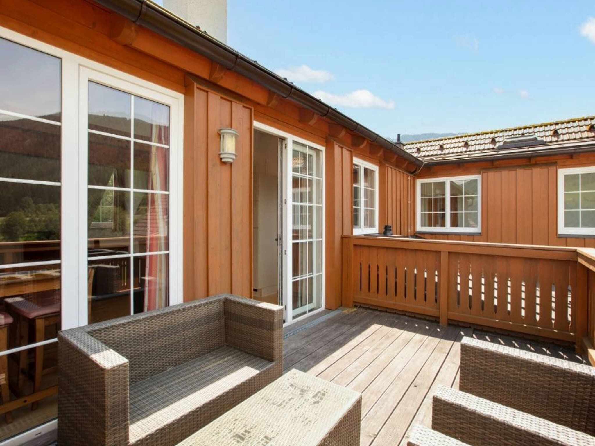 Una terraza de madera con mobiliario de mimbre y una valla de madera.