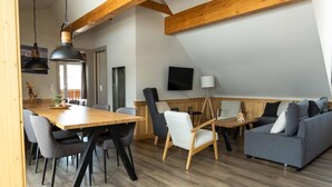 Un espacio habitable moderno estilo loft con comedor, un conjunto de sofás y un televisor montado en la pared.