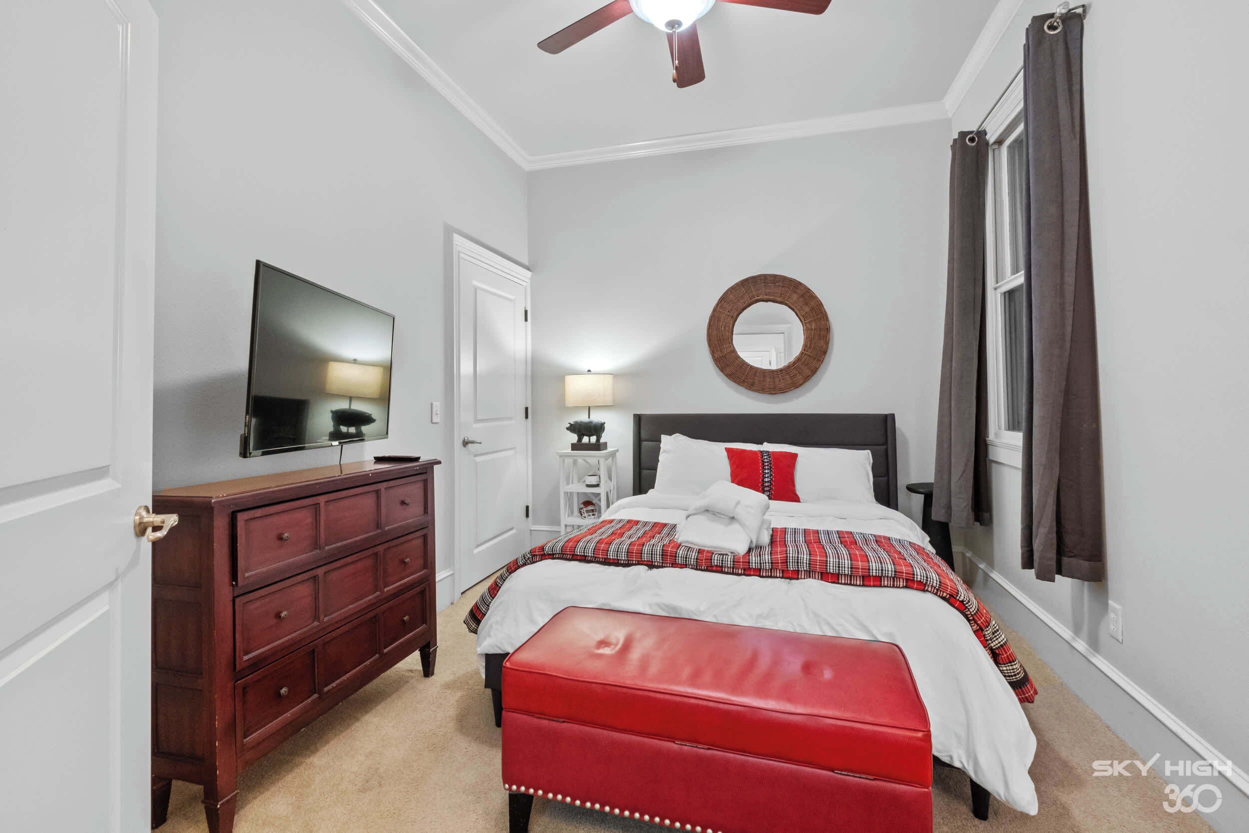 Een slaapkamer met een bed, een dressoir, een spiegel en een plafondventilator.