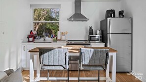 A compact kitchen with a central island, a stainless steel range hood, a refrigerator, and a microwave.