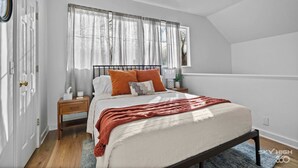 A bedroom with a bed, nightstands, a window with sheer curtains, and a view of trees outside.