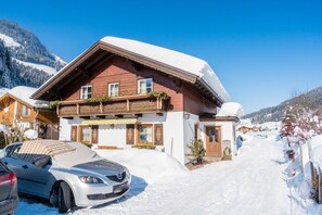 Een houten chalet met een met sneeuw bedekte dak, een auto ervoor geparkeerd, en een berg op de achtergrond.