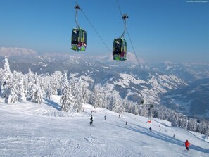 Un télésiège avec des cabines suspendues à des câbles, un paysage montagneux enneigé et des skieurs sur les pistes.