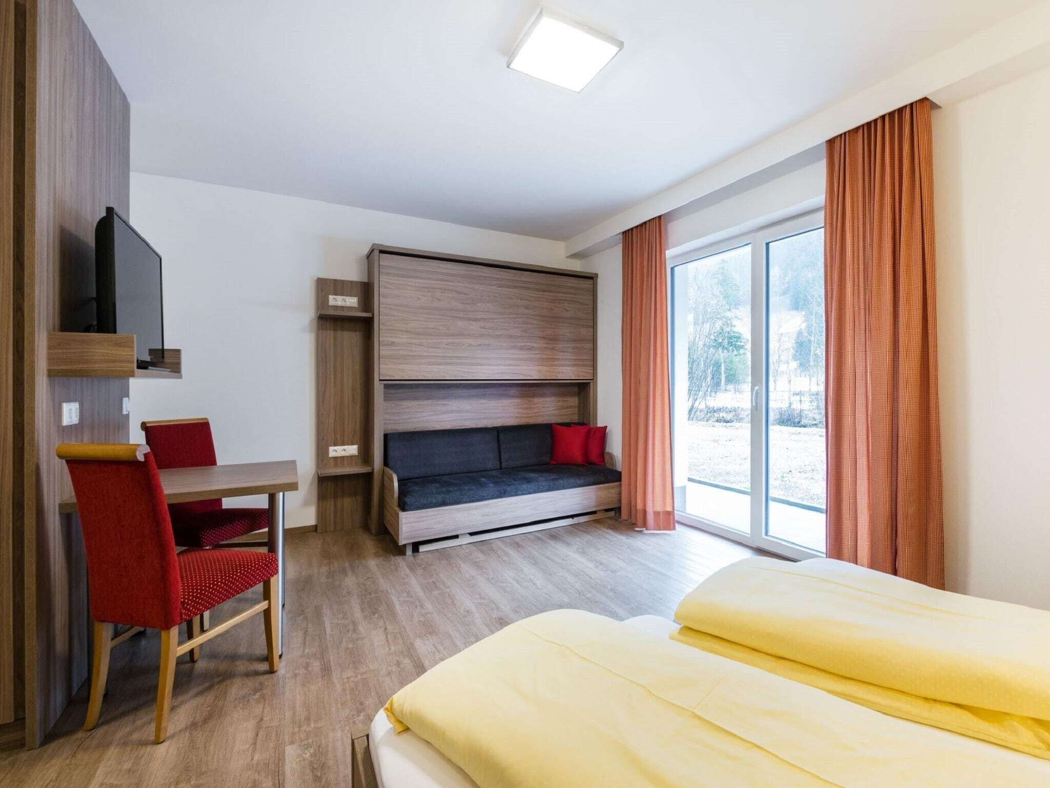 Een moderne hotelkamer met een bed, een bureau, een stoel, een bank en een aan de muur bevestigde televisie.