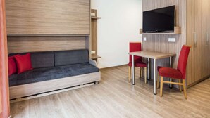 Un espace de vie compact comprenant un canapé, un téléviseur fixé à un meuble en bois et une petite table à manger avec des chaises.