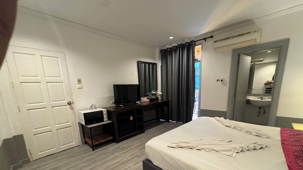 A hotel room with a bed, a desk with a TV, a microwave, and a bathroom with a sink and mirror. - Stay At Bedroom (Patong)