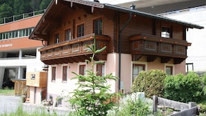 A traditional wooden chalet with a balcony, surrounded by lush greenery and a modern building in the background. - Chalet in Dienten on Hochkönig Ski Slopes (Dienten)