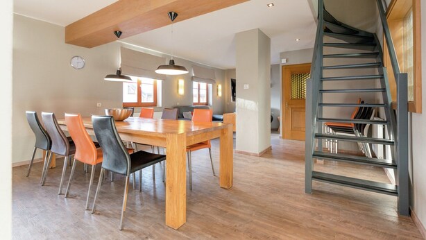 A spacious dining area with a wooden table and chairs, a staircase with a glass railing, and a clock on the wall. - Chalet in Dienten on Hochkönig Ski Slopes (Dienten)