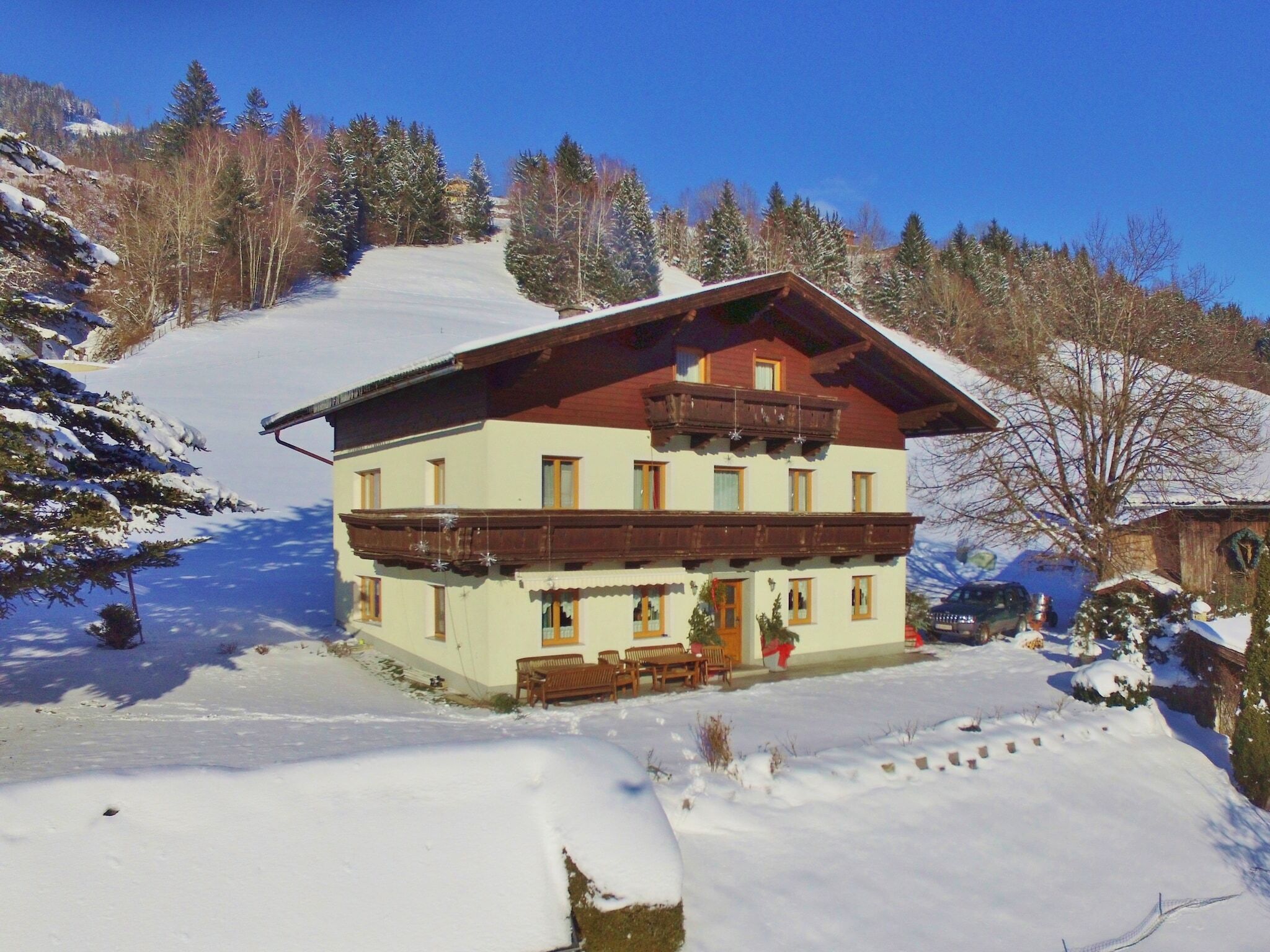 A multi-story chalet with a wooden balcony, surrounded by snow-covered trees and a clear sky.