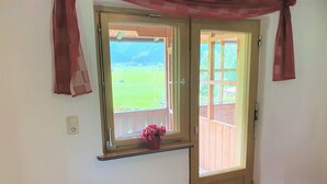 A room with a wooden door and a window with a view of a wooden deck and greenery.
