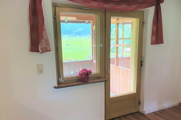 A room with a wooden door and a window with a view of a wooden deck and greenery.