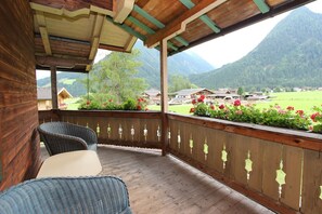 A wooden deck with wicker furniture and a view of a village and mountains.