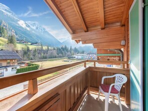 Ein Holzbalkon mit Blick auf eine Berglandschaft, ein Stuhl und ein Gebäude im Hintergrund.