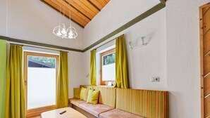 Ein gemütliches Zimmer mit Holzbalkendecke, einer Couch mit gestreiften Kissen, einem Holztisch und einem Fenster mit Vorhängen.